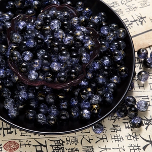 Macro detail of 10mm deep purple cracked glass beads with gold patterns in a black bowl