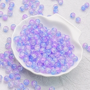Macro detail of 10mm purple and blue gradient crackle glass beads in a white shell dish
