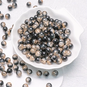 Detailed macro view of 10mm black and gold crackle glass beads in a ceramic shell dish
