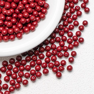 Dunkelrote runde Zinnober-Perlen für DIY-Schmuck auf einer weißen Keramikplatte