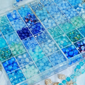 24-grid organizer filled with assorted blue DIY glass beads and handmade jewelry sets