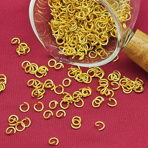 Golden open jump rings for DIY jewelry making scattered on luxury red fabric background