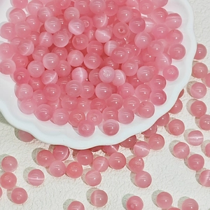 Macro view of round pink cat eye glass beads for DIY jewelry making in a white ceramic dish