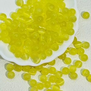 Close-up of vibrant yellow cat eye glass beads for DIY jewelry making in a white dish