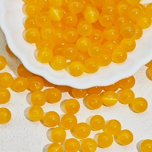 Close-up of bright orange cat eye glass beads for DIY jewelry making in a white dish