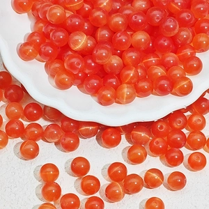 Detailed macro view of orange cat-eye glass beads for DIY jewelry making in a white bowl