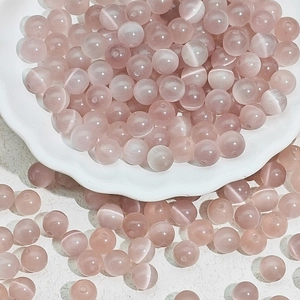Detailed view of pink cat eye glass beads in a white bowl for DIY jewelry making