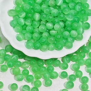 Close-up of green cat eye glass beads for DIY jewelry making on white petal tray