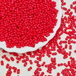 Macro detail of red twin-hole peanut glass beads for DIY jewelry in a white ceramic dish