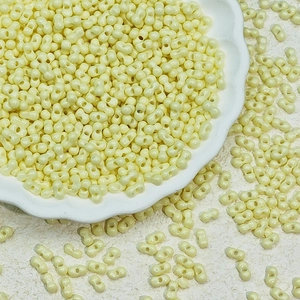 Pale yellow 3x6mm two-hole peanut glass beads displayed on a white floral plate