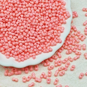 Macro detail of 3x6mm pastel pink glass seed beads in a white porcelain dish
