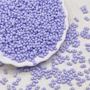 Macro detail of lavender double-hole glass beads for DIY jewelry on white porcelain plate
