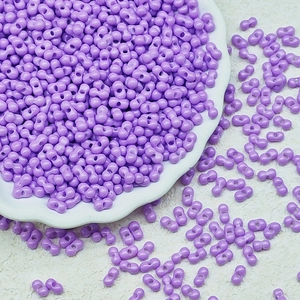 Detail of lilac purple two-hole peanut glass beads in a white ceramic dish
