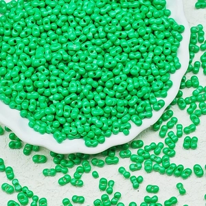 Macro shot of 3x6mm green peanut glass beads for jewelry making in white ceramic dish