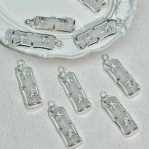 Detailed view of bamboo-shaped white resin charms with silver floral relief for DIY jewelry