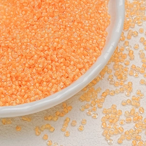Macro detail of peach orange 3mm glass seed beads in a white bowl for DIY jewelry
