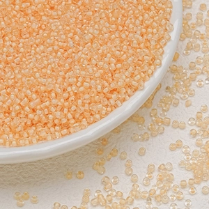 Detailed macro view of 3mm apricot glass seed beads in a white ceramic dish for DIY jewelry