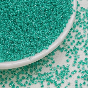 Macro shot of 3mm teal glass seed beads for DIY jewelry making on white background