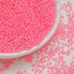 Macro shot of 3mm bright neon pink glass seed beads in a white bowl for DIY jewelry