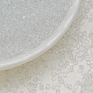 Macro shot of 3mm transparent glass seed beads on a white porcelain dish for jewelry DIY