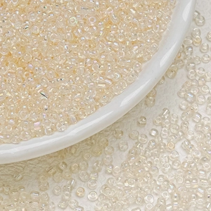 Macro shot of 3mm iridescent cream glass seed beads on a white porcelain dish and leather