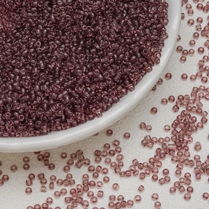 Macro shot of 3mm purple glass seed beads in a white ceramic dish for DIY jewelry