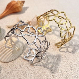 Modischer offener Armreif mit Blumenmuster in Gold und Silber auf Strandsand