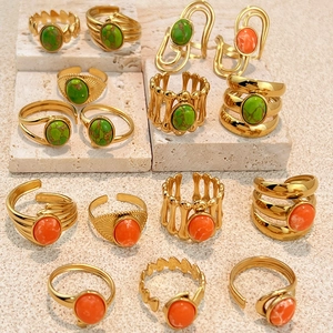Bagues en acier inoxydable doré serties de pierres vertes et orange sur pierre beige