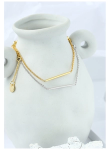 Dettaglio di bracciali minimalisti in oro e argento con pendente a barra su vaso bianco