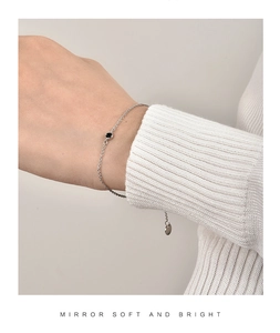 Detail eines minimalistischen Silberarmbands mit schwarzem Zirkon auf Strickhintergrund