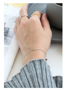 Dettaglio di un bracciale a barra in argento e anelli a onde con un maglione grigio
