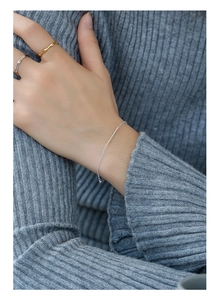 Dettaglio di un bracciale a catena e anello in argento indossati su un maglione grigio