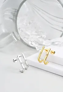 Close-up of minimalist J-shaped gold and silver earrings with centered cubic zirconia