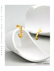 Macro detail of J-shaped gold-plated stud earrings with center diamond inlay on display