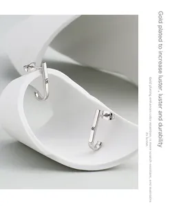 Detail of silver J-shaped stud earrings with inlaid zircon on minimalist white sculpture
