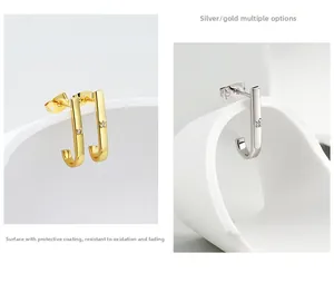 Detail of J-shaped metal stud earrings in gold and silver finish with sparkling zircon