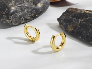 Detailed view of thick 18K gold plated huggie hoop earrings on natural stone background