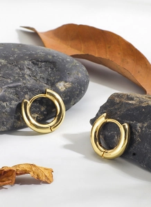 Detailed close-up of 18K gold plated hoop earrings on minimalist stone and leaf background
