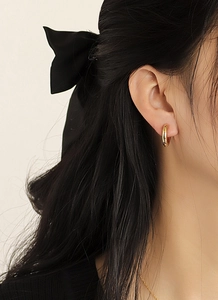 Close-up of elegant gold plated round hoop earrings worn by a model with a black bow