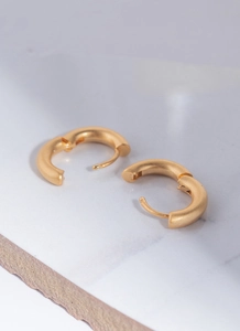 Detail of matte 18K gold plated huggie hoop earrings on a light marble stone surface