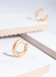 Detail of chunky gold huggie hoop earrings with matte finish on marble stone background