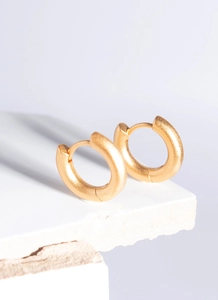Detailed close-up of matte gold huggie earrings on a white stone texture background