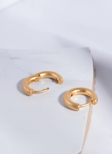 Close-up of matte 18K gold plated hoop earrings showing hinged clasp on marble surface