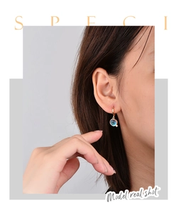 Detail of gold geometric hoop earring with blue translucent pendant and micro zircon
