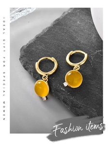 Close-up of golden round drop earrings with yellow resin stone and zircon on stone plate
