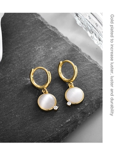 Macro shot of gold plated earrings with white opal stone and zircon on stone texture