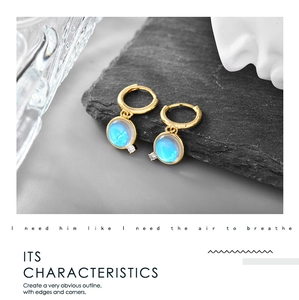 Detail of gold hoop earrings with light blue moonstone pendant and a white accent stone