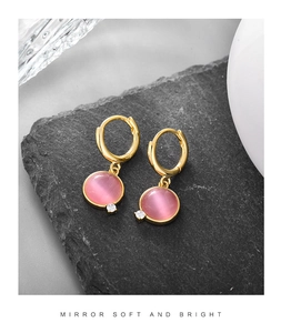 Macro detail of gold hoop earring with round pink cat eye stone and white zircon on stone
