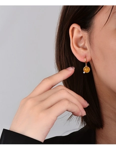 Detailed close-up of a gold geometric earring with amber stone and zircon on female ear