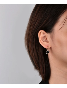 Close-up of gold geometric earrings with black round stone inlay and small crystal accent